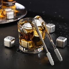 a glass filled with ice cubes next to a metal spoon and some silver objects