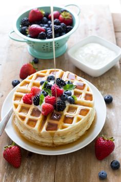 a waffle topped with berries and blueberries sits on a plate next to a bowl of yogurt