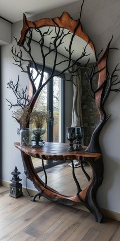 a mirror sitting on top of a wooden table next to a tree branch design in front of a window