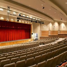 an empty auditorium with rows of seats and a red curtain on the front wall,