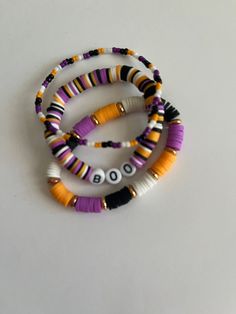 three bracelets with beads are sitting on a white surface and one is purple, the other is yellow