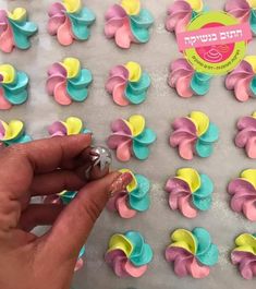 a hand is pointing at some colorful icing on a sheet of tin foil with flowers