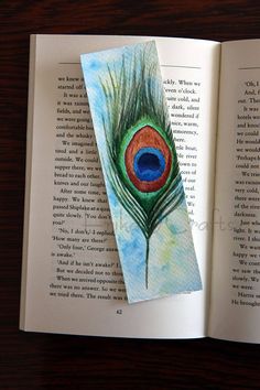 an open book with a peacock feather on it's cover and the pages are painted in watercolor