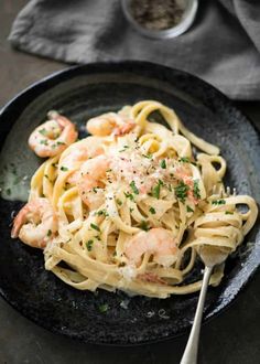 pasta with shrimp and parmesan cheese in a black bowl next to a fork