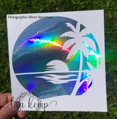 a person holding up a sticker with a palm tree and rainbow in the background