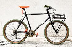 a black bike with orange rims parked next to a white wall and drain grate