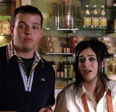 a man and woman standing in front of a shelf with bottles on the shelves behind them