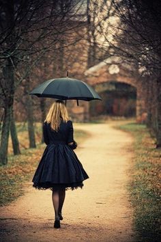 a woman walking down a dirt road holding an umbrella