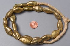 "A strand of handmade rustic brass beads from Ghana. Each is made one at a time - the Diamond Bicone shape is so interesting for tribal jewelry and rest comfortably on the neck. A favorite 21 beads 21\" of beads - 26\" overall 25x15x10mm on average 2-3mm hole" Artisan Bronze Beaded Necklaces With Polished Beads, Adjustable Gold Beaded Necklaces With Wooden Beads, Handmade Metal Beads In Gold, Adjustable Artisan Gold Beaded Necklaces, Artisan Gold Beaded Necklaces With Spacer Beads, Artisan Brass Jewelry With Large Beads, Brass Beaded Necklaces With Gold Beads, Handmade Gold Metal Beads, Artisan Gold Beaded Necklaces For Festivals