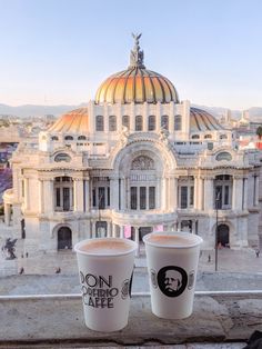 two coffee cups sitting on top of a window sill in front of a building