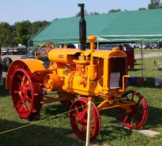 an old yellow and red tractor sitting in the grass