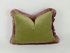 a green and pink pillow with fringe trim