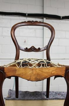 an old chair with nails on the back and seat is sitting in front of a white brick wall