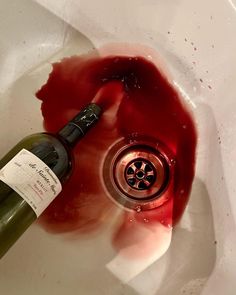 a bottle of wine sitting in a sink with red liquid pouring out of the faucet