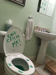 a white toilet sitting in a bathroom next to a sink with green lettering on it