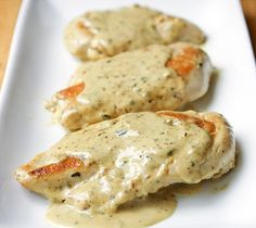 two pieces of chicken covered in gravy on a white plate with a wooden table