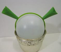 a white ball with green ears sitting in a silver cup