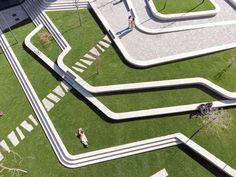 an aerial view of people walking on the grass in front of a building with stairs