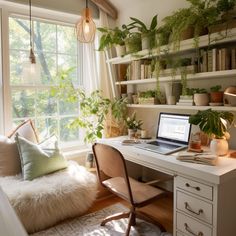 a laptop computer sitting on top of a white desk next to a plant filled window