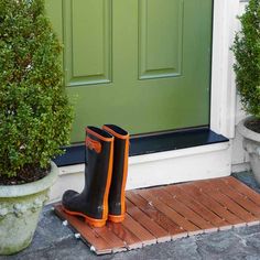 a pair of rubber boots sitting on top of a wooden mat next to a green door