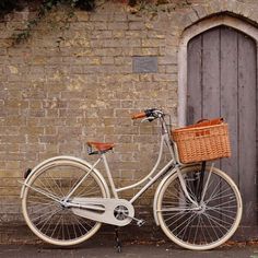 a white bicycle parked next to a brick wall with a basket on the front wheel