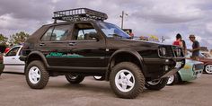 a black truck with a rack on the roof parked in a parking lot next to other cars