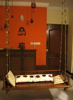 a wooden swing bed with pillows on it in a room that has an orange wall