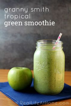 a green smoothie in a mason jar next to an apple on a blue napkin