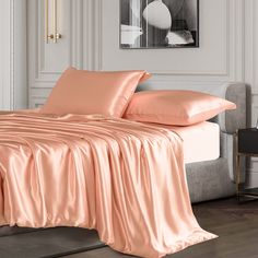 a bed with pink sheets and pillows in a white room next to a painting on the wall