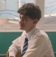 a young man wearing a shirt and tie sitting at a table