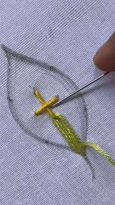 someone is stitching the cross on a piece of fabric with yellow thread and scissors