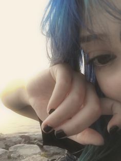 a close up of a person with blue hair and black nail polish holding their hand to her face