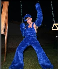 a man dressed as a blue monster swinging on a swing set at night with his hands in the air