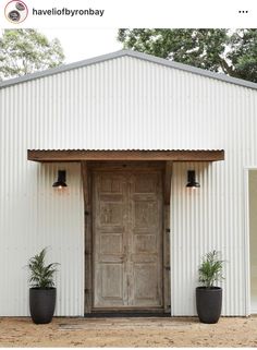 a white building with two large black planters on the front and one big wooden door