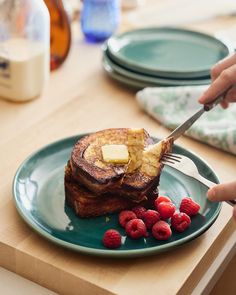 a person is cutting into some french toast with butter and raspberries on the plate