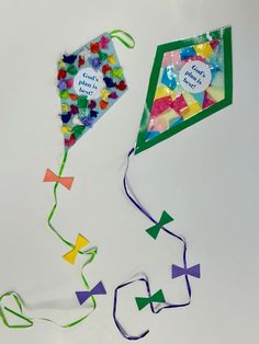 two kites that are next to each other on a white surface, one is decorated with confetti and the other has a message