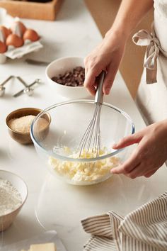 a woman mixing ingredients in a bowl on top of a white table with other bowls and utensils