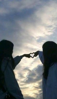 two girls making a heart shape with their hands in front of the sky at sunset