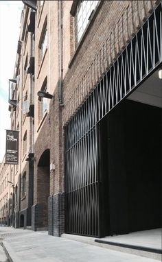 an alleyway with brick buildings and metal bars on the doors, in front of a black gate