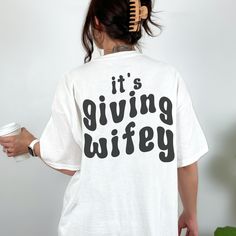 a woman wearing a white t - shirt that says it's giving wiffy