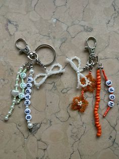 two key chains with beads and letters on them sitting on a marble counter top next to each other