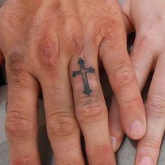 two people holding hands with tattoos on their fingers and one has a cross tattooed on the middle finger