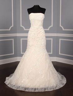 a white wedding dress on display in a room with gray walls and wooden floors,