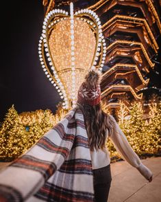 a woman is walking in front of a building with christmas lights on it and a blanket draped around her