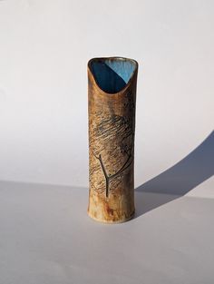 a wooden vase sitting on top of a white table next to a shadow cast wall