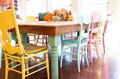 a wooden table surrounded by colorful chairs and pumpkins on top of the dining room table