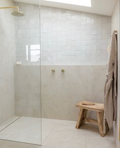 a walk in shower sitting next to a wooden bench under a skylight on top of a tiled floor