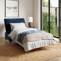 a bed with white sheets and blue headboard in a bedroom next to a window