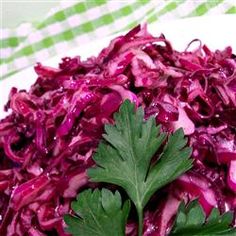 a white plate topped with red cabbage and green leafy garnishments on top of a checkered table cloth