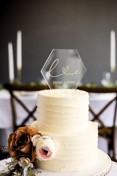 a white wedding cake with flowers on the side and an acrylic name plate